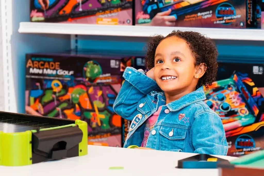 A girl smiling and laughing while playing arcade mini golf inside a Go! Toys and Games store