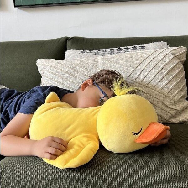 A child sleeping soundly on a couch hugging a giant yellow Snoozimal duck plush