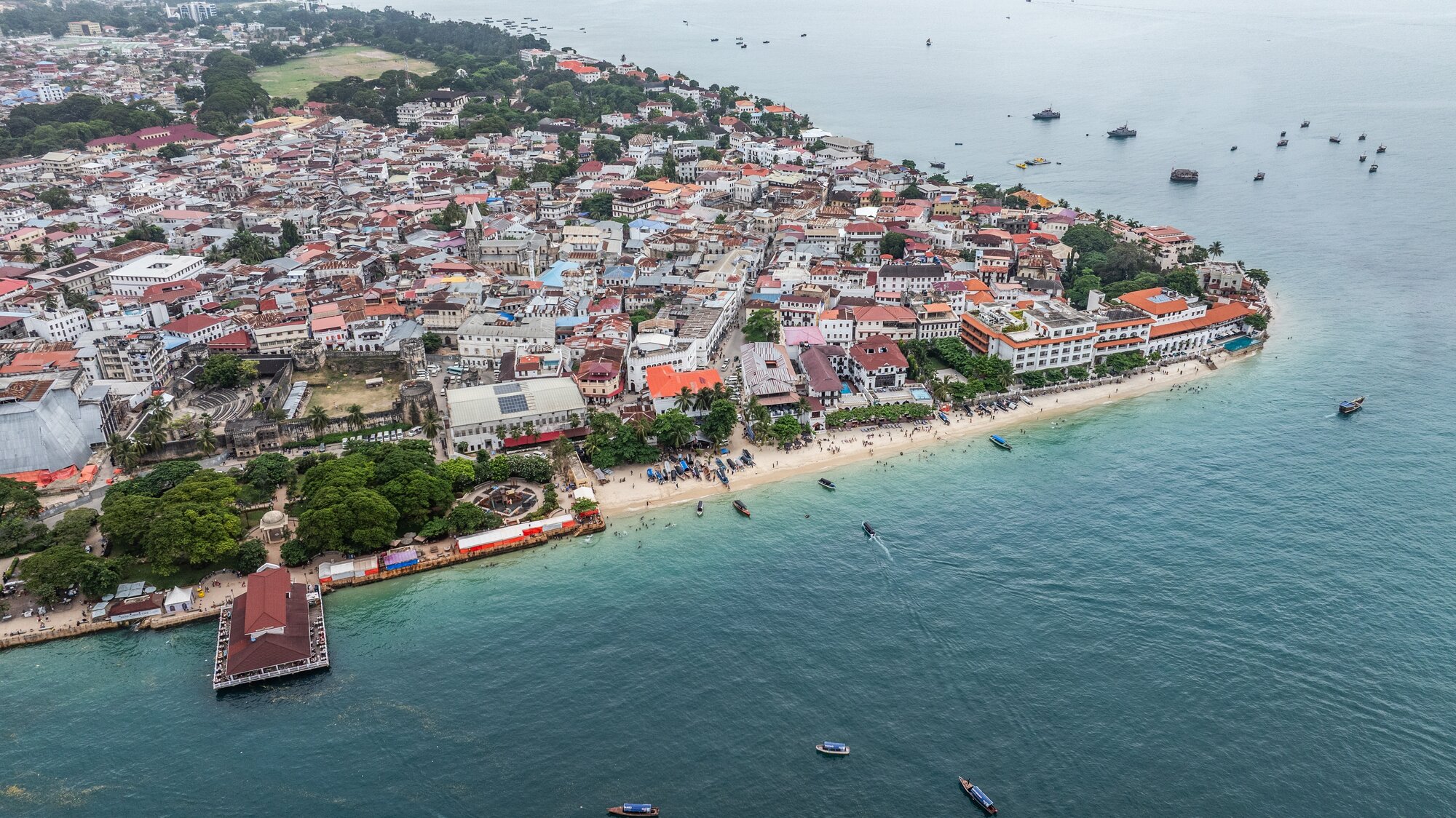 Aerial landscape view of the tip area of historic Stone Town, the oldest part of Zanzibar Town on Unjuja island, Tanzania with historic buildings and beaches - many boats anchored along coastline 