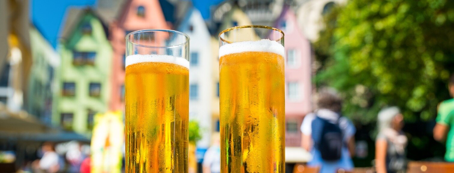 Two glasses of beer on a table in front of buildings in Cologne, Germany