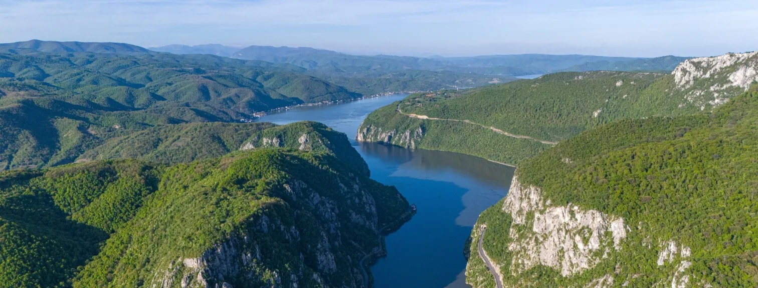 Aerial view of the Iron Gates Gorge on the Danube River, marking the border between Serbia and Romania. Towering cliffs and forested hills frame the deep canyon in the heart of the Balkans.