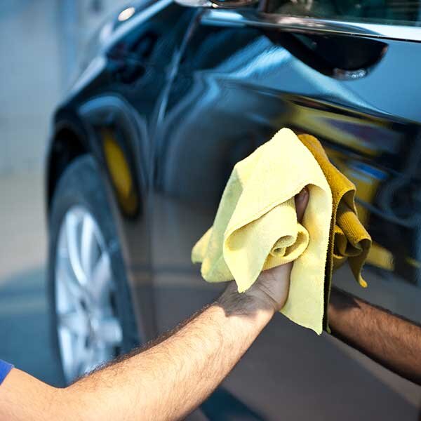 A hand cleaning the exterior of a black sedan.