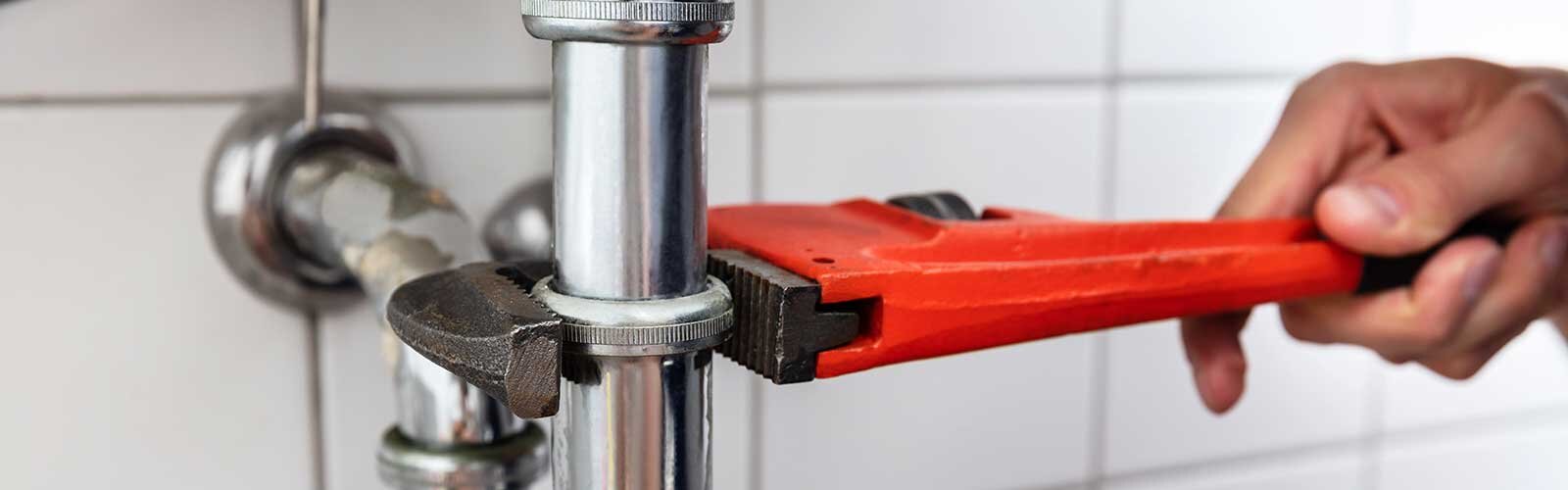 A plumber uses a wrench on a pipe under the sink.