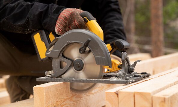 A person sawing lumber with a yellow cordless circular saw.