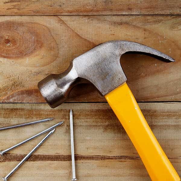 A hammer with a yellow handle lays on a wooden surface.