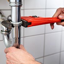 A person using a wrench under the sink.