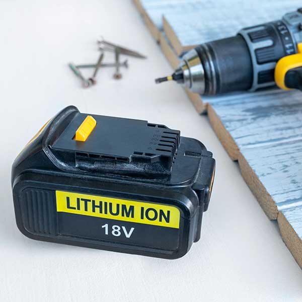 A battery for a power tool lays besides wooden slates and a drill.