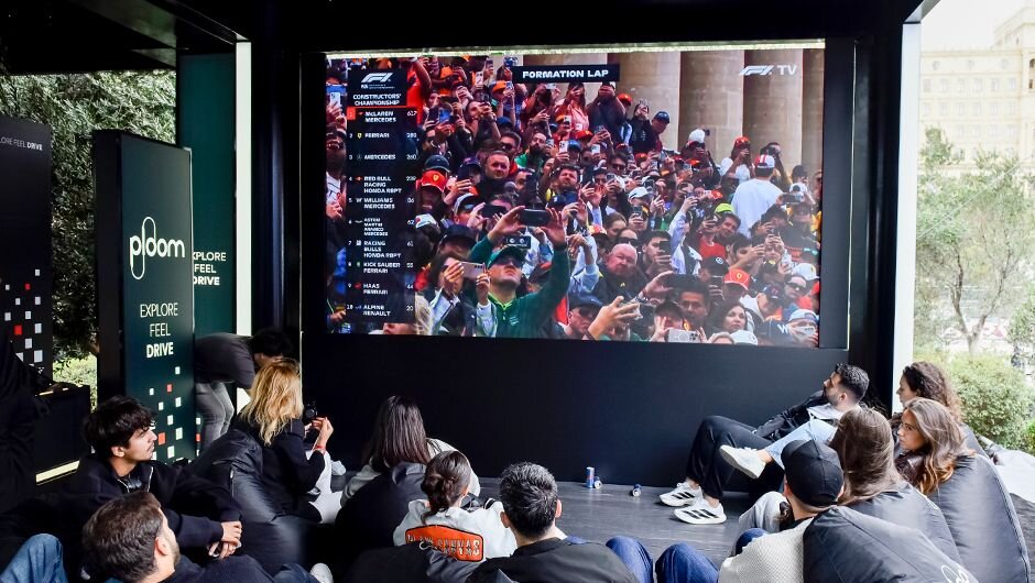 Azarkeşlər Ploom zonasındakı böyük ekranda Bakı Yarışı 2025-in canlı yayımını izləyir, rahat beanbag oturacaqlarda festival ab-havasını yaşayır. 