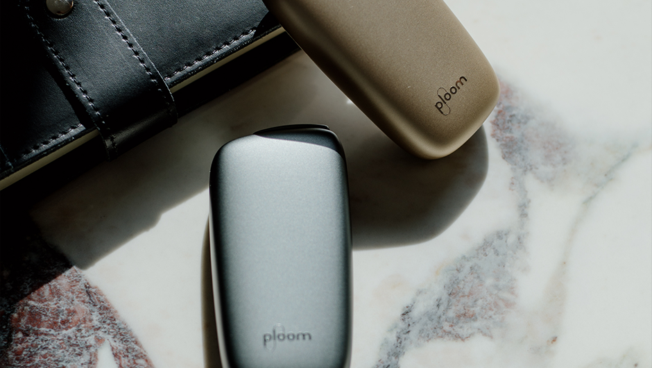 Mərmər üzərində qızılı və gümüşü Ploom cihazları, dəri qeyd dəftəri ilə birlikdə