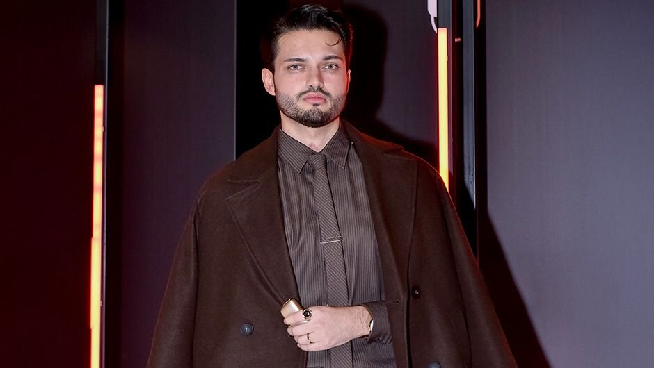 Ploom tədbirində qəhvəyi tərzdə geyinmiş kişi modeli Ploom cihazını təqdim edir. 