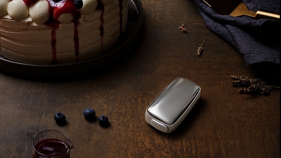 A Ploom device on a table next to a chocolate and fruit cake.