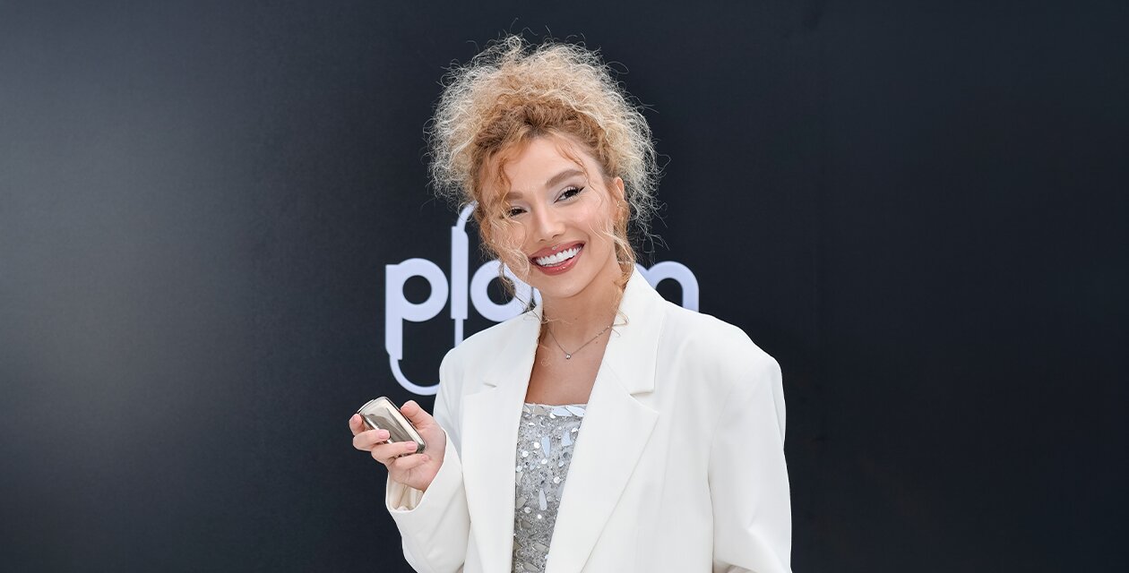 Uzel Karimova, smiling in a white jacket, holding a Ploom device in her hand