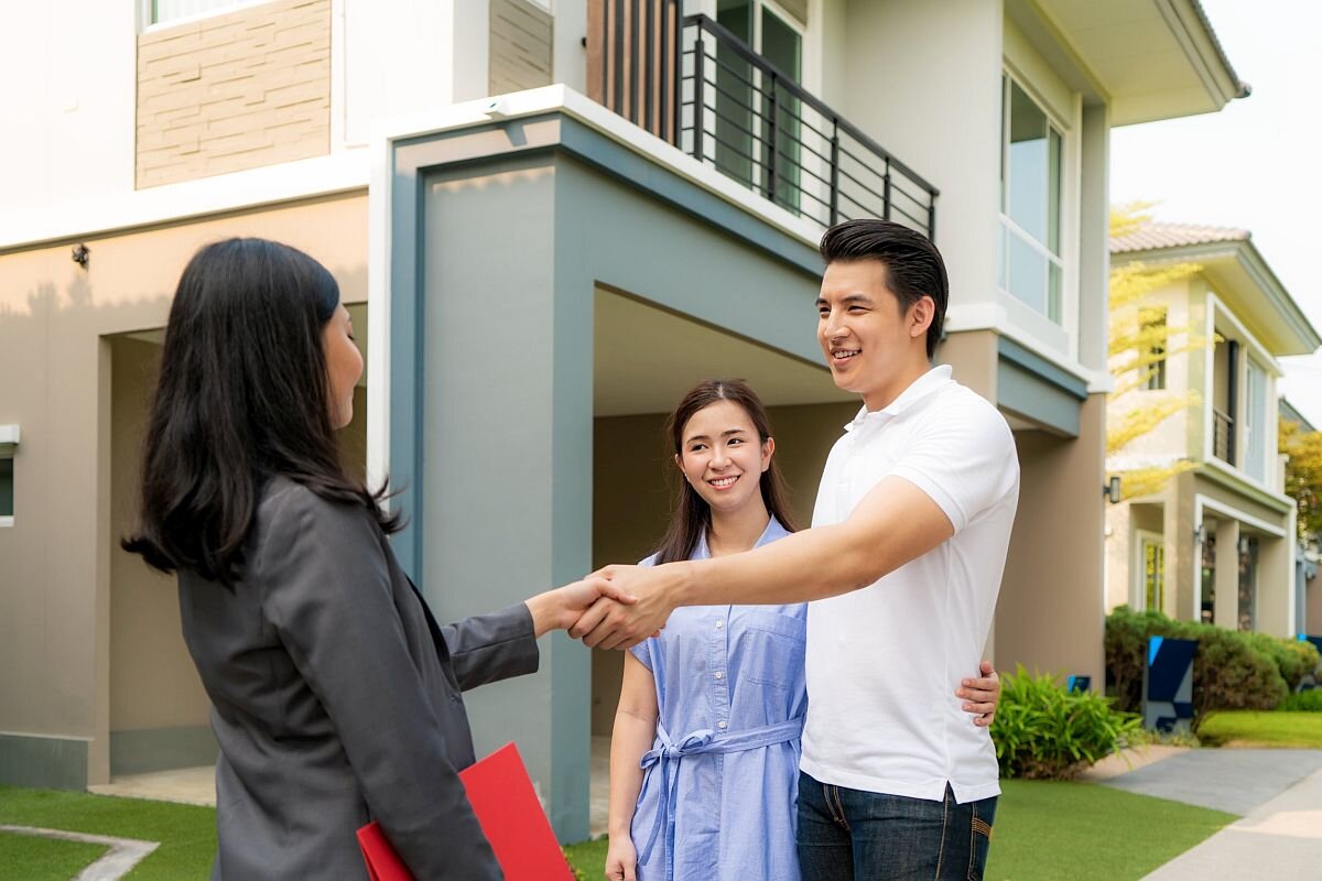 Happy Asian couple looking for their new house and shake hands with real estate broker after a deal. Young couple handshaking real estate agent after signing contract for buy house.