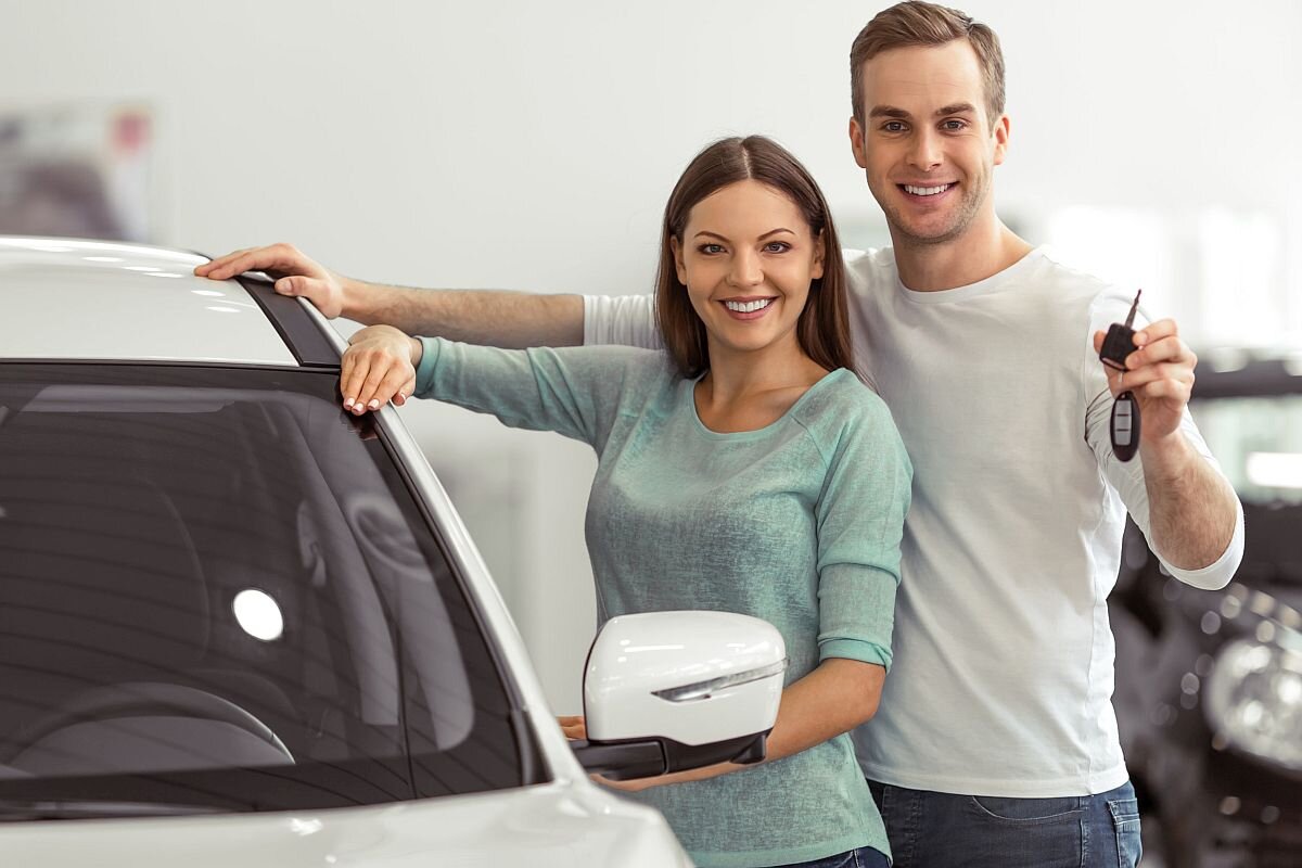 young couple leaning on their new car in a motor show