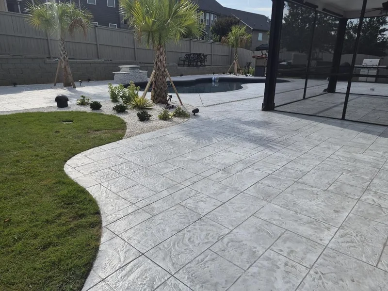 Gray stamped concrete pool deck and patio with a curved lawn edge