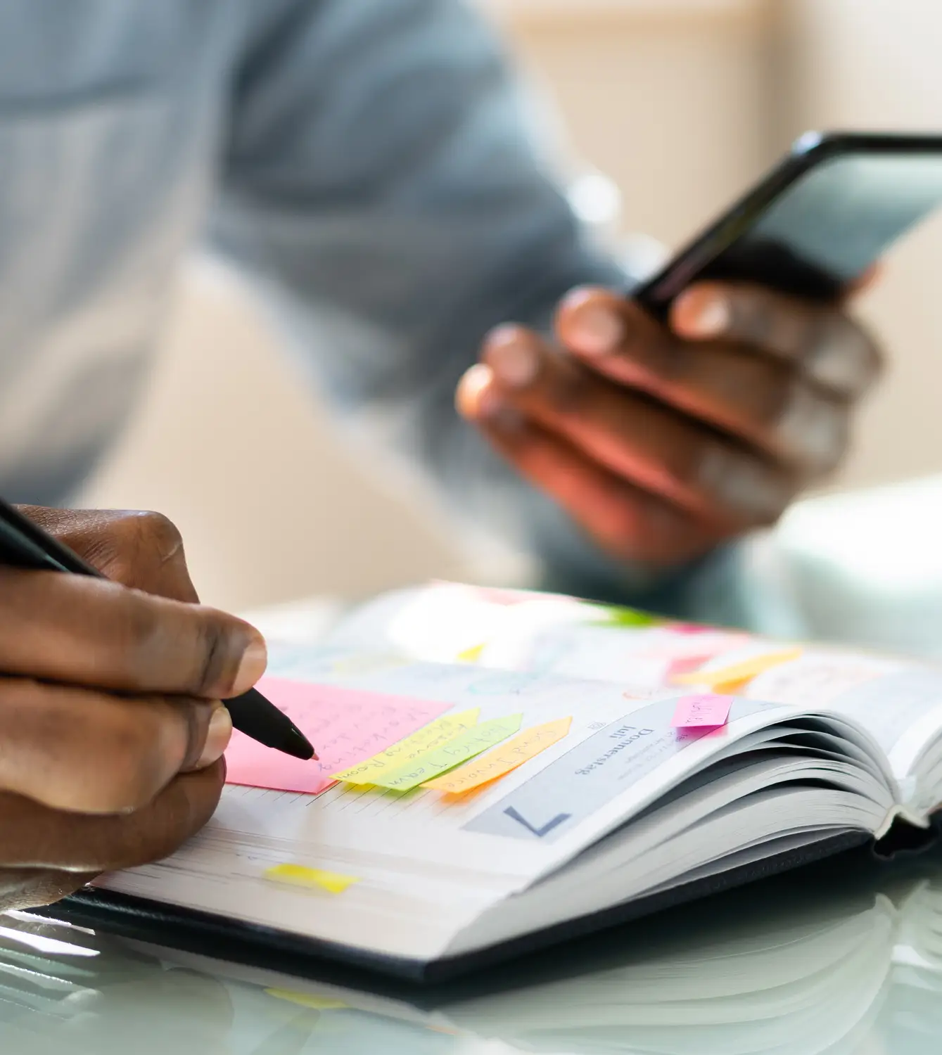 A woman working at a black desk, in a white office, on the phone and writing on some paper.