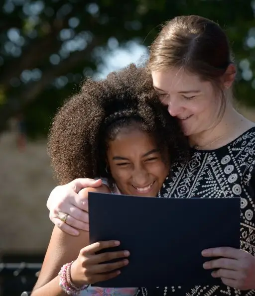 A young student and teacher smiling, both holding a black card, embracing.