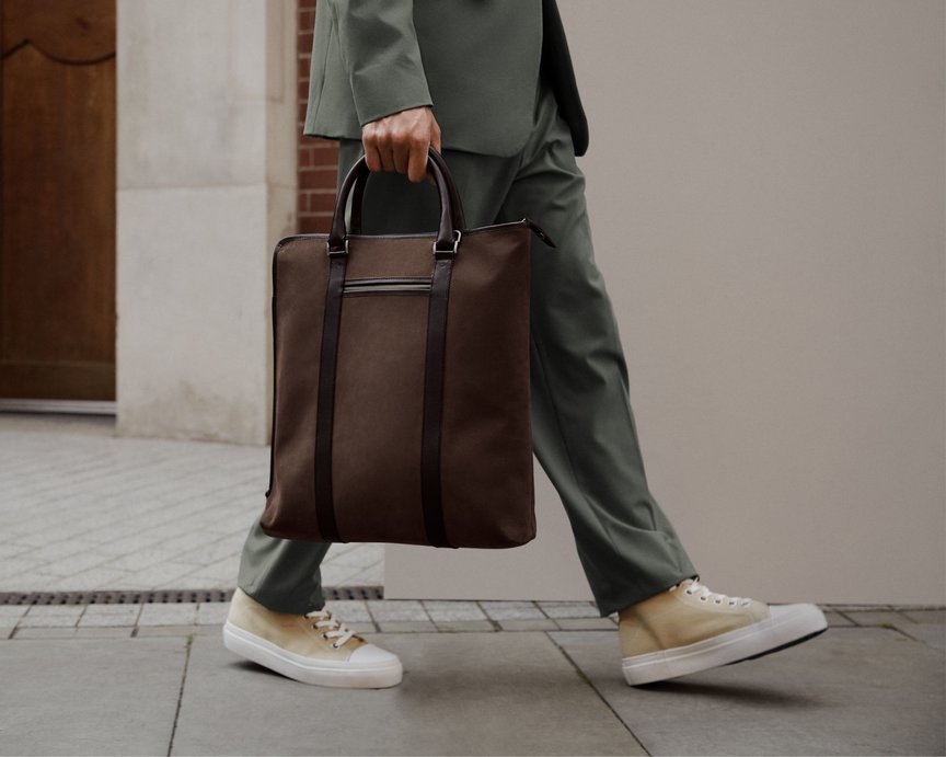 Model in green suit and yellow trainers walks holding brown nubuck leather tote bag 