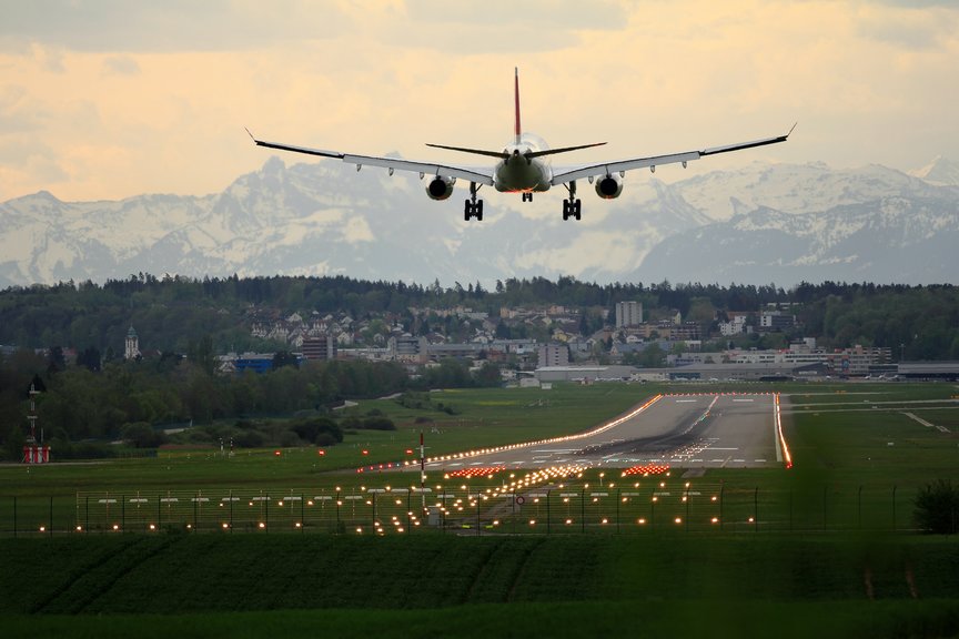 Plane landing on airstrip with mountains and greenery in background