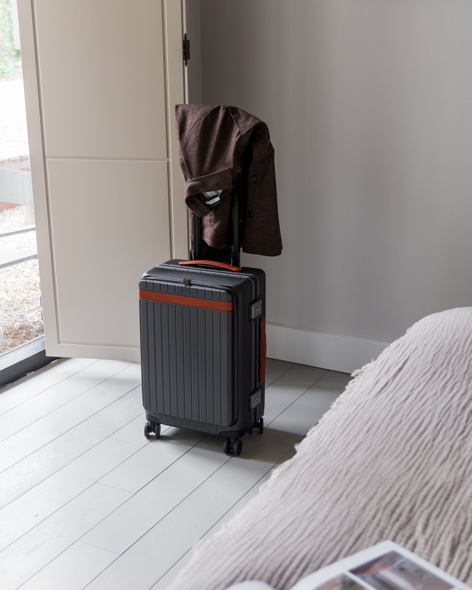 Brown collared jacket hanging off the handle of a grey hard-shell cabin suitcase