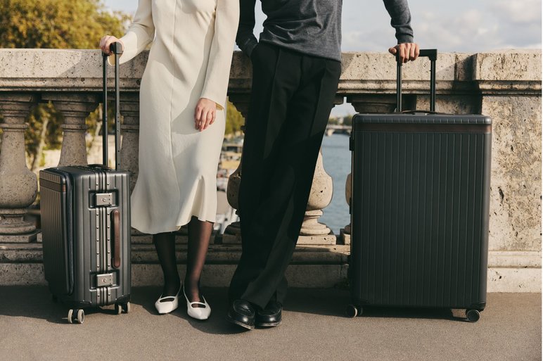 Man and women lean on Parisian bridge holding two stylish suitcases 