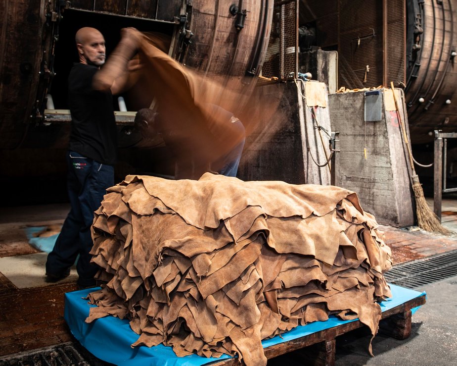 Man adds a soft brown leather hide to a pile in a tannery
