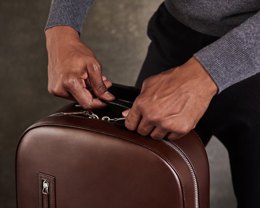 Model opening the zips of a premium leather brown backpack, designed by Carl Friedrik