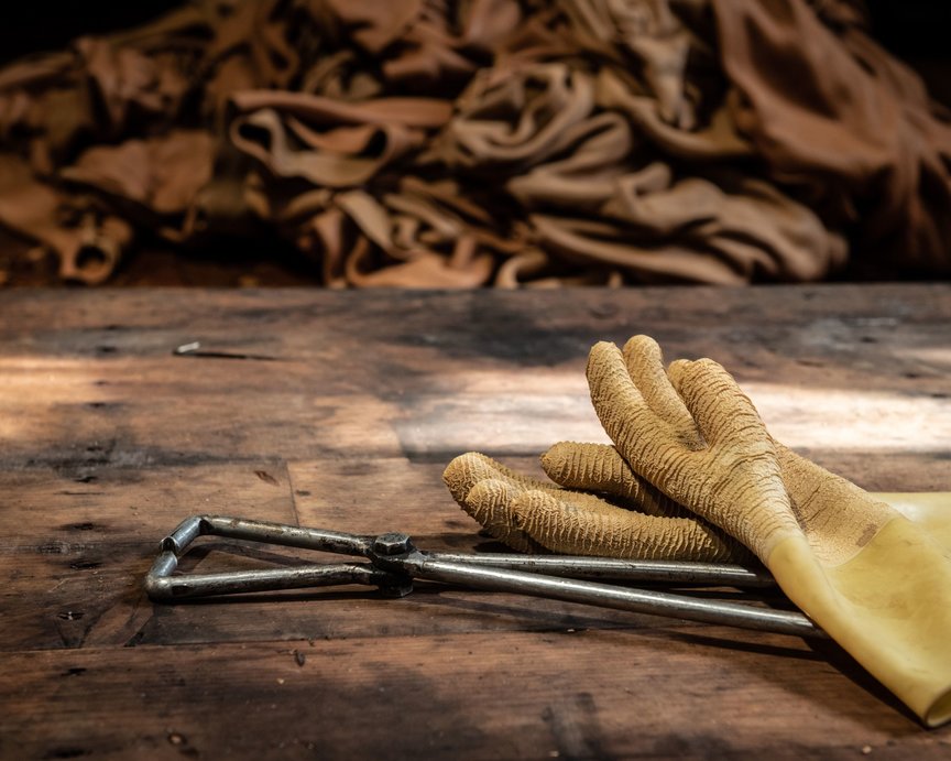 Inside of a tannery showing raw animal hides, leather tool and yellow work gloves.