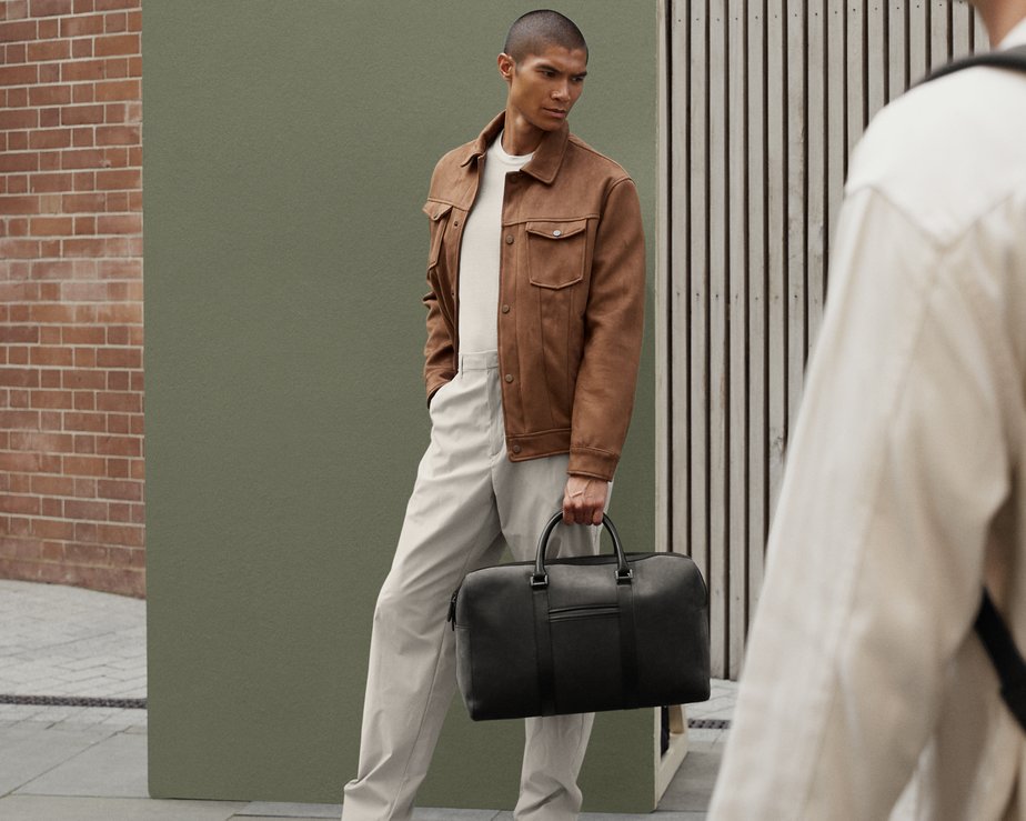 Stylish model in white top and brown overcoat holds suave nubuck weekend bag