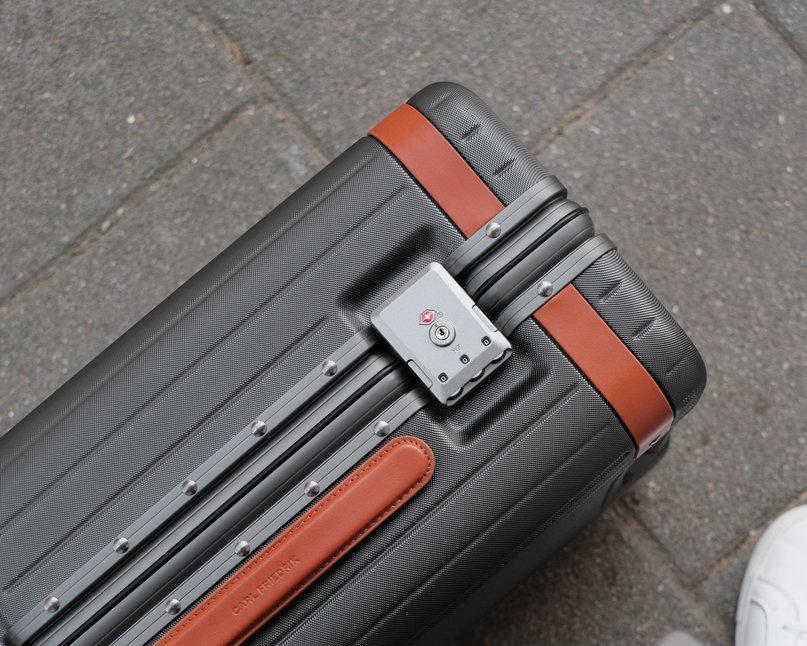 Grey polycarbonate suitcase with Italian leather detailing resting on floor