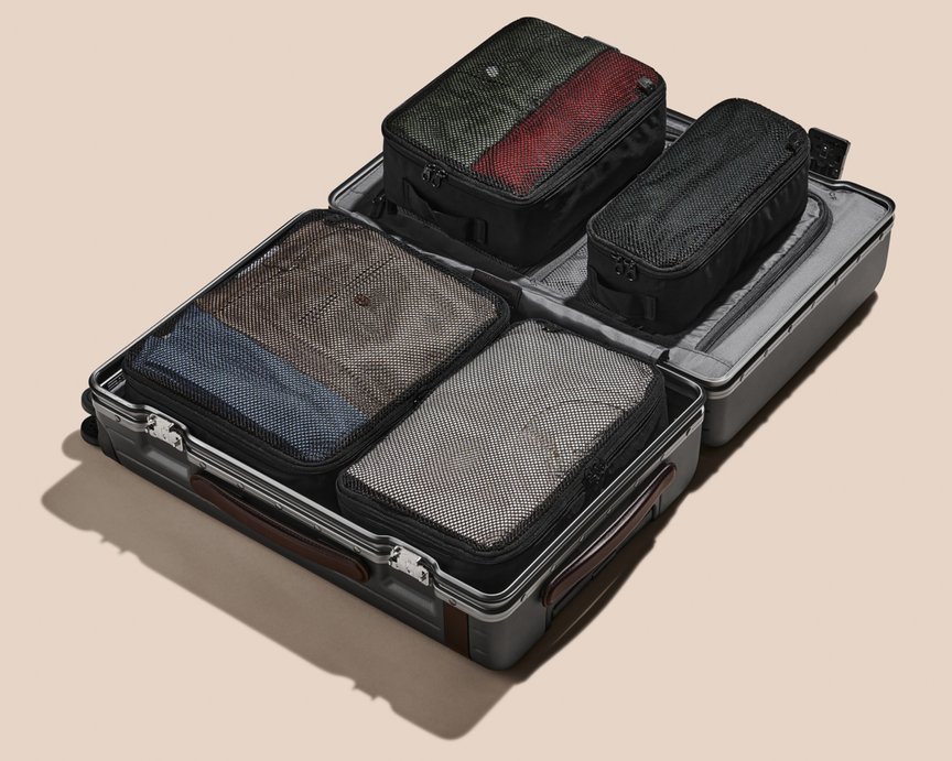 Four Carl Friedrik packing cubes resting in a sleek carry-on suitcase