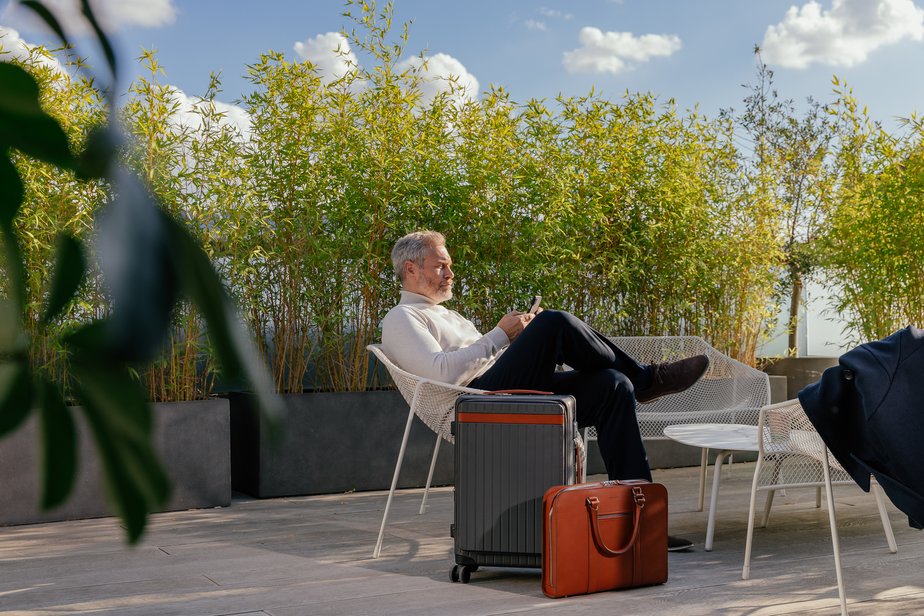 Smartly dressed man sits on balcony beside luggage with London skyline in background