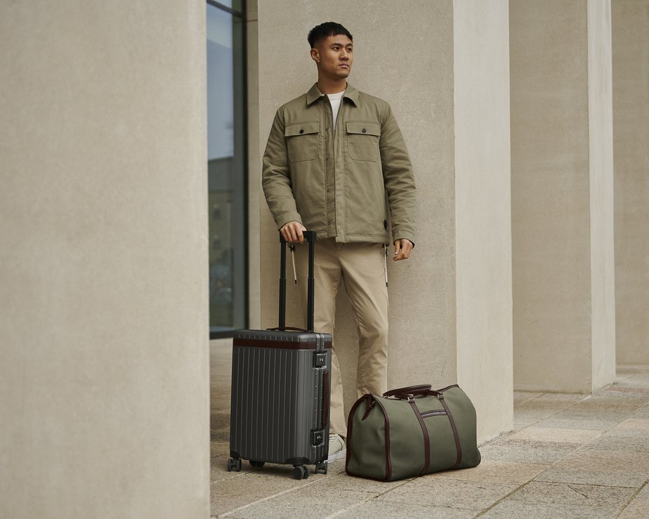 Man standing beside grey carry-on suitcase and green weekend bag