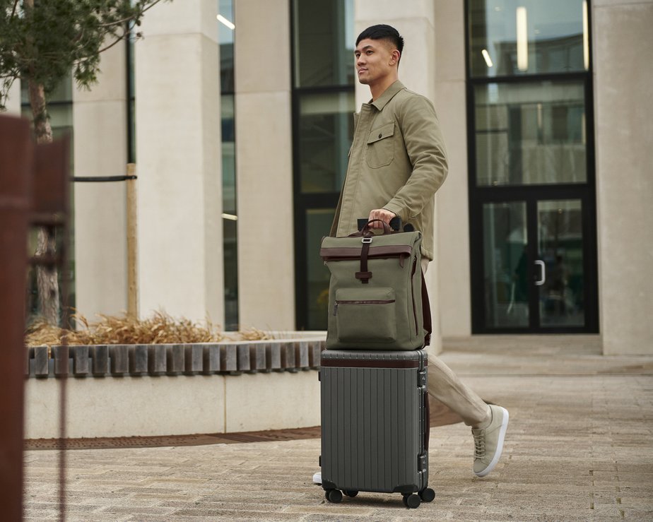 Model walking with grey polycarbonate carry-on suitcase with green backpack on top