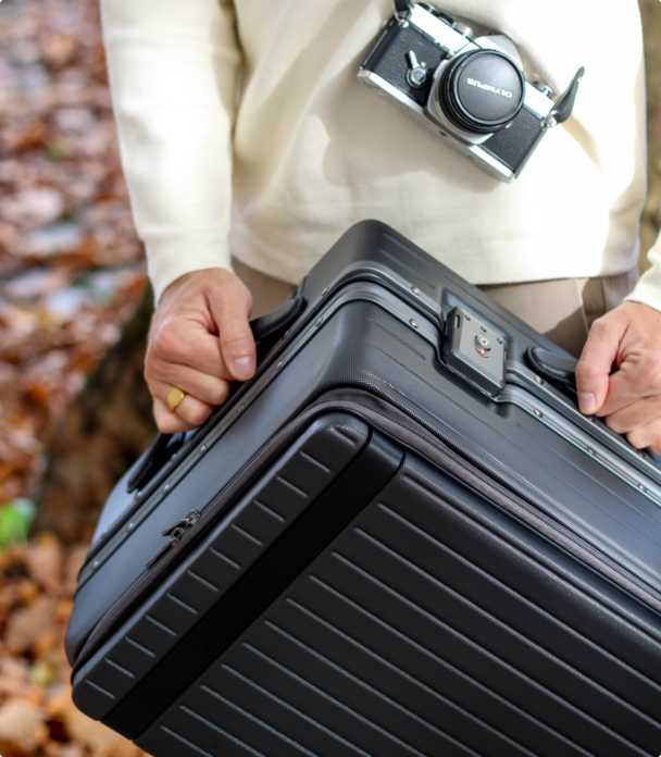 Bleisure traveller holding grey carry-on suitcase with camera round his neck