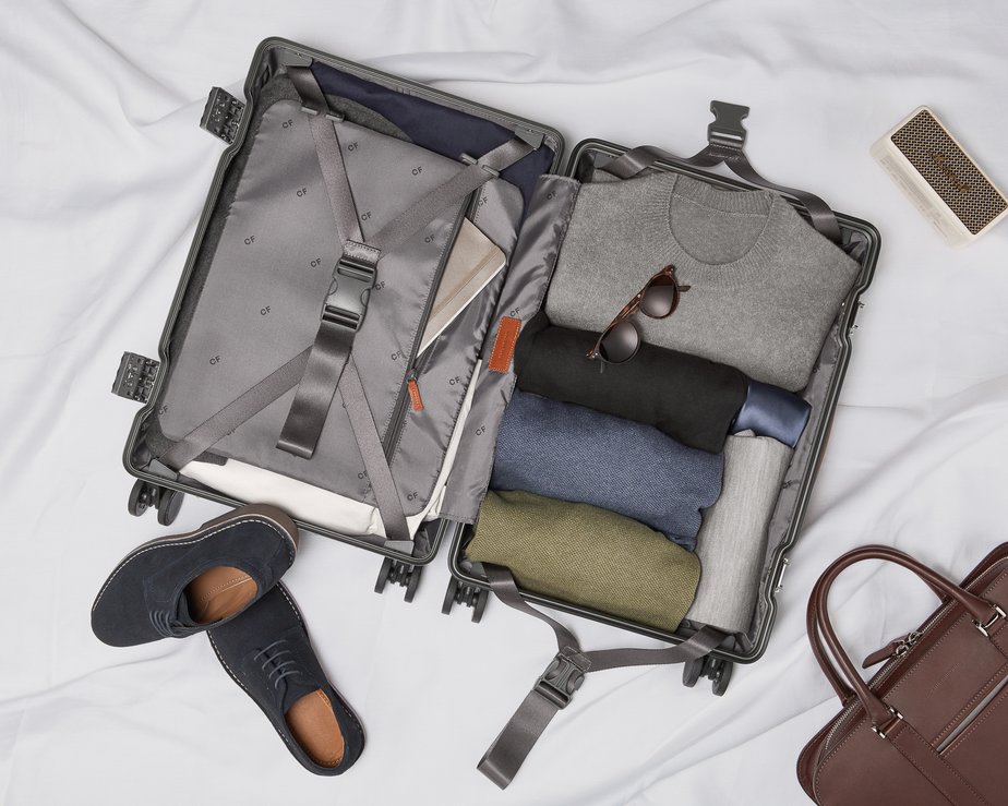 Open suitcase with clothes neatly folded inside and shoes and bag beside it