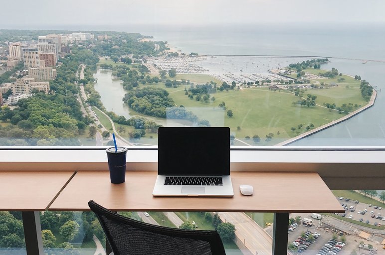 Desk with MacBook on it overlooks parkland and coastline below