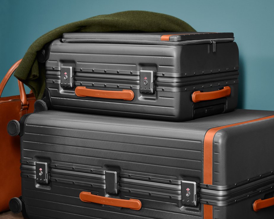 Two grey polycarbonate suitcases of varying sizes stacked with a green jumper ontop