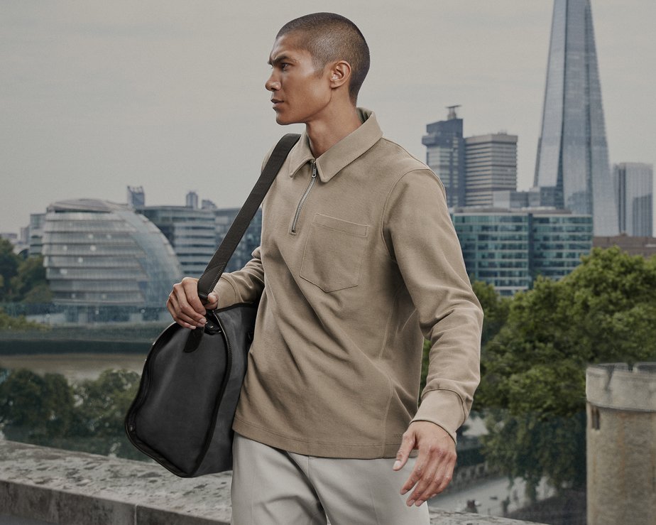 Man holding grey duffel bag with London skyline behind