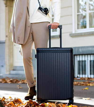 Bleisure traveller walking beside grey check-in suitcase wearing beige suit