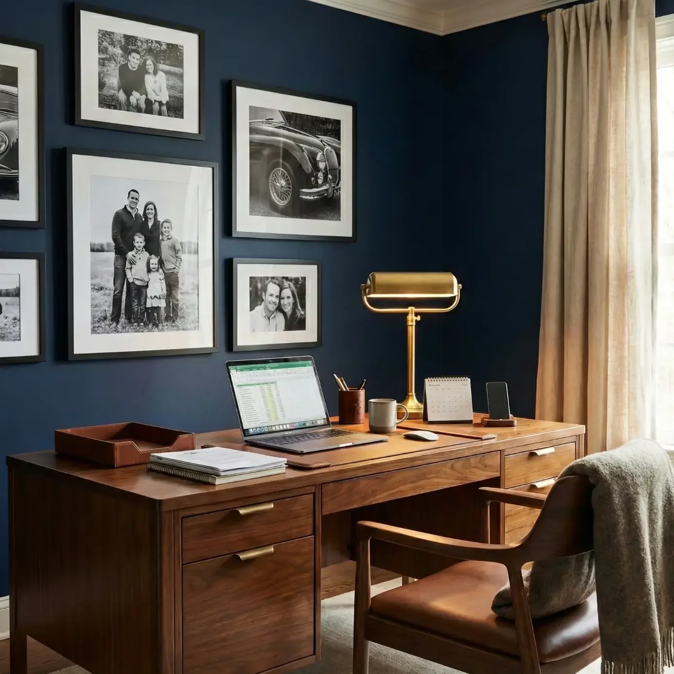 Home office with navy walls, gallery frames, and wood desk