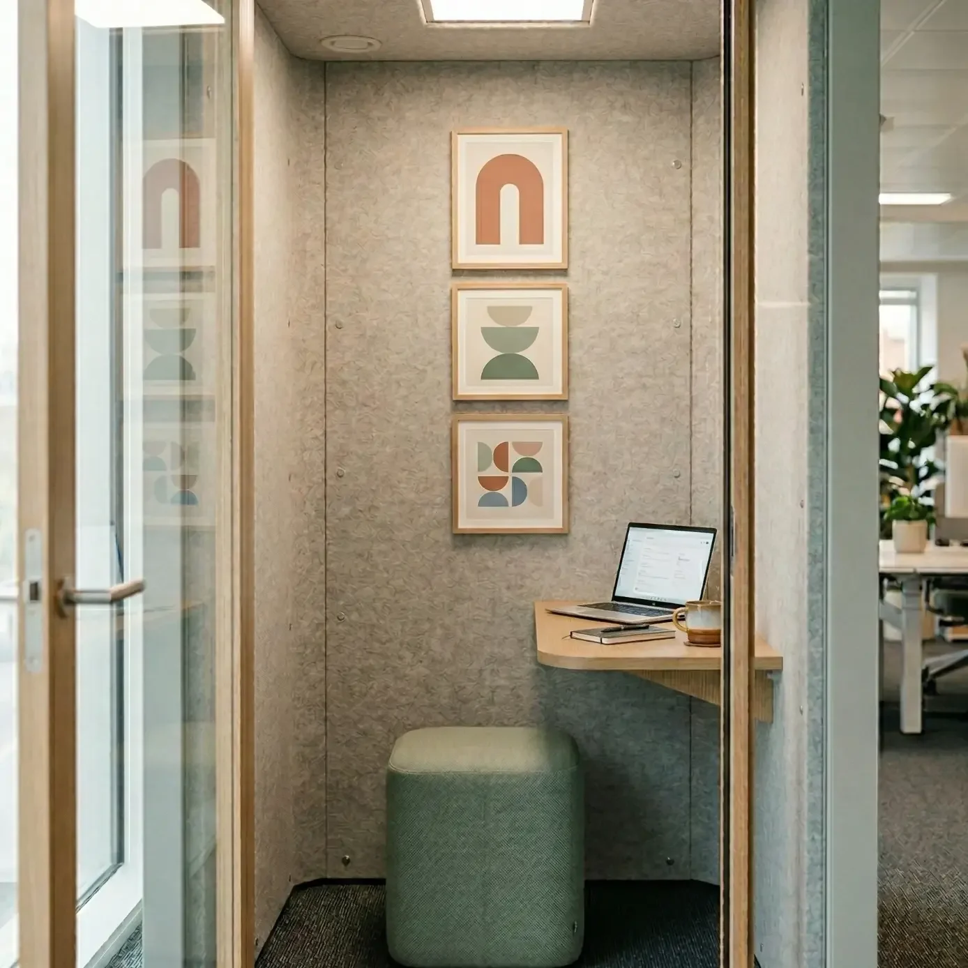 Private phone booth workspace with laptop, shelf desk, and art