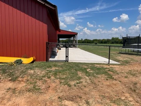 Fenced property beside a red barn and concrete pad