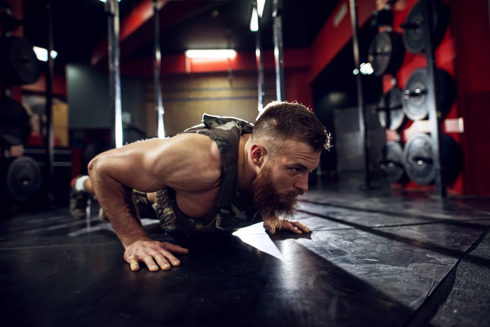 Portrait close up view of strong motivated muscular bearded short hair bodybuilder man doing push ups on the floor in the dark gym.