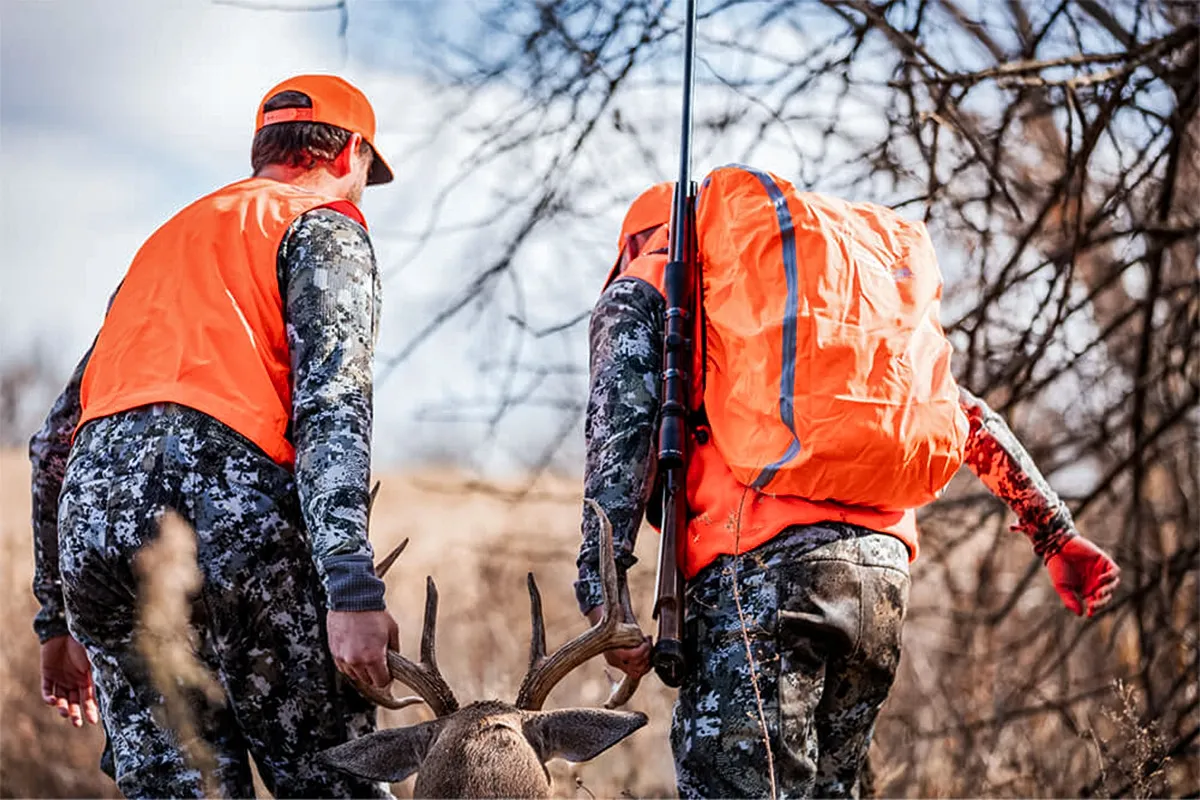 Hunters wearing orange drag deer out of the woods