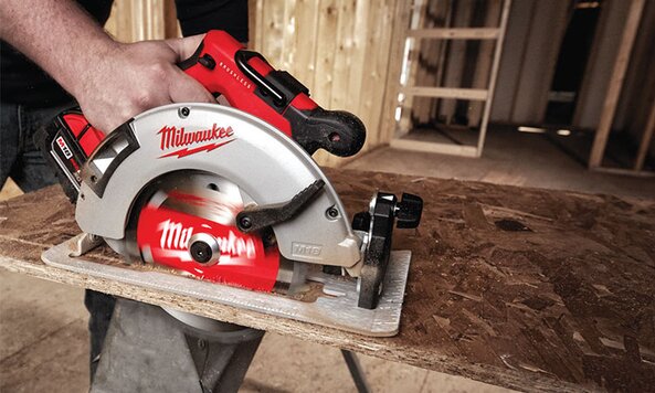 A Milwaukee cordless circular saw is being used to cut a piece of plywood. 