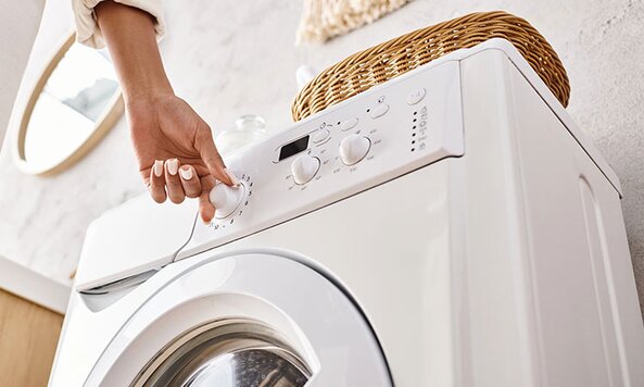 A woman's hand turning the dial on a white front-load washer. 