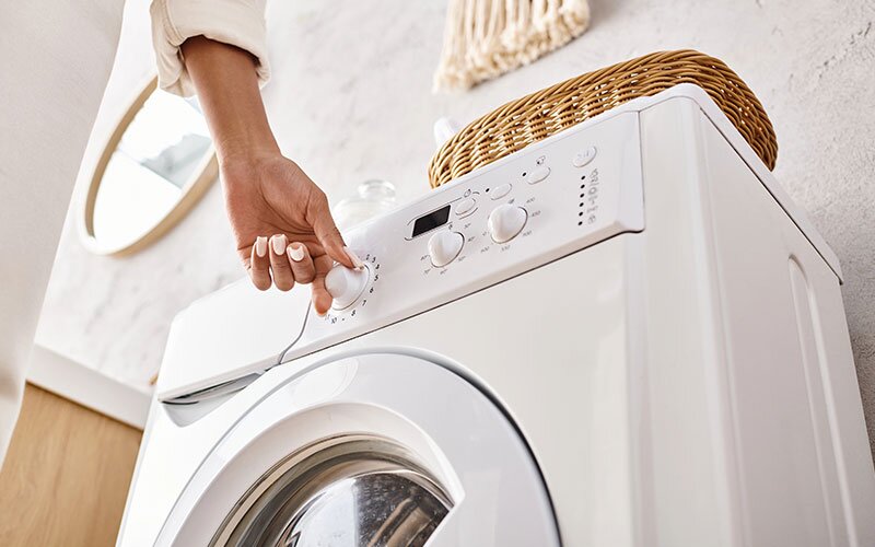 A homeowner turning the dial on their front-load washer.