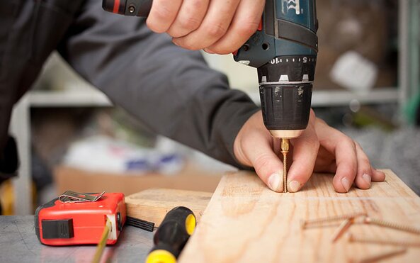 A person drilling a screw into a piece of wood.
