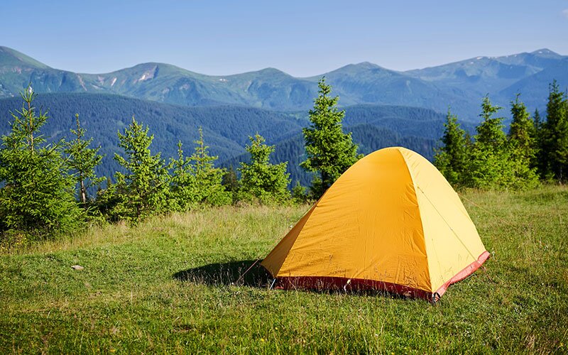 A yellow tent pitched in a field overlooking mountains. 